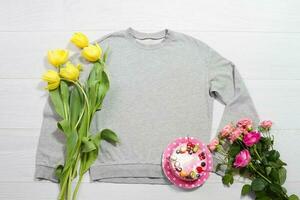 fermer gris Vide modèle sweat-shirt sweat à capuche copie espace. les mères femmes journée Jaune tulipes, rose des roses, gâteau. content anniversaire Haut vue maquette arrêtez-vous. blanc en bois Contexte. plat allonger modèles photo