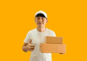 Jeune asiatique livraison homme portant casquette et blanc Vide T-shirt en portant parcelle Publier boîte isolé sur Jaune Contexte. Express livraison un service concept. photo