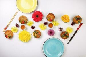 coloré fleur décoré lune gâteau chinois milieu l'automne Festival thé dans petit blanc tasse à thé baguettes assiettes bleu Jaune violet chrysanthème maman rouge Marguerite fleur sur blanc Contexte photo