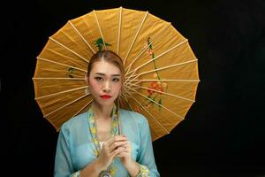 asiatique femme dans tractionnel kebaya derrière parapluie sur noir Contexte photo