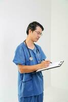Jeune asiatique Masculin médecin portant tablier uniforme tunique stéthoscope écrire presse-papiers photo