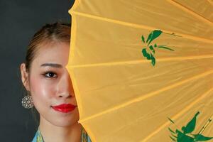 asiatique femme dans tractionnel kebaya derrière parapluie sur noir Contexte photo