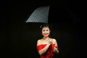 asiatique femme dans moderne rouge robe en dessous de parapluie sur noir Contexte photo