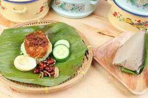 nasi Lemak parfumé riz cuit dans noix de coco Lait servi avec sambal ami cacahuète anchois bouilli Oeuf emballé dans banane feuille sur rond bambou assiette sur en bois Contexte photo