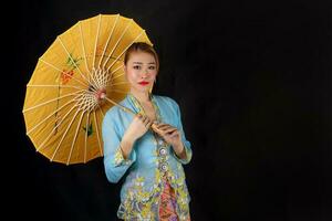 asiatique femme dans tractionnel kebaya porter parapluie sur noir Contexte photo