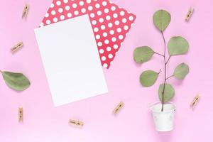 Un brin avec des feuilles dans un seau blanc avec une carte de voeux blanche sur fond rose uni photo