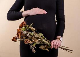 Vue latérale d'une jolie femme enceinte caressant son ventre et tenant un bouquet de roses sèches