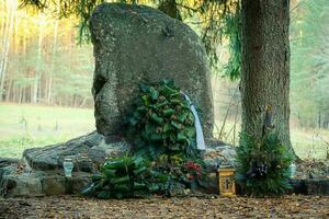 pierre tombale permanent grand dans cimetière avec gros fleur couvrant près arbre avec brillant ensoleillé Prairie derrière il photo