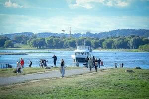 kaunas, Lituanie 20 dix 2022 petit blanc navire à venir à le rive sur rivière bleu l'eau tandis que gens sont effrayant sur le rivière banque sur ensoleillé journée photo