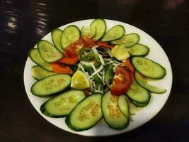 Frais fait maison biologique vert salade dans blanc assiette avec noir Contexte photo