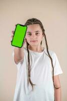 Jeune fille montrant téléphone intelligent avec vert écran isolé sur beige Contexte photo