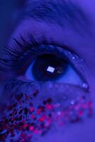 extrême fermer vue de femelle œil avec brillant maquillage avec scintille illuminé rose bleu néon lumière photo