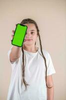Jeune fille montrant téléphone intelligent avec vert écran isolé sur beige Contexte photo