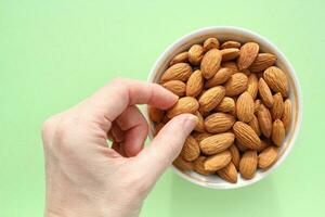 amande sur blanc céramique bol et main de femme sur vert Contexte. en bonne santé en mangeant régime, nutrition, végétalien concept. protéine biologique aliments. sec collation. nationale écrou journée. copie espace pour texte photo