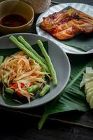 thaïlandais nourriture plat tous les deux dans Thaïlande et Asie, Papaye salade ou comme nous appel il somtum est complété avec grillé poulet et gluant riz avec Frais sautés. servi sur le noir en bois tableau. photo