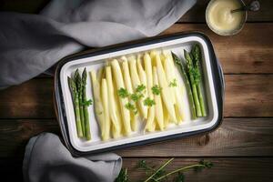 traditionnel à la vapeur blanc asperges avec Hollandaise sauce et herbes comme une Haut vue dans un émail plateau sur un vieux bois table avec copie espace sur le droite, produire ai photo