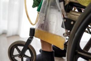 Femme asiatique patiente assise sur un fauteuil roulant avec sac d'urine dans la salle d'hôpital photo