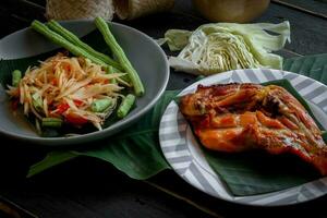 thaïlandais nourriture plat tous les deux dans Thaïlande et Asie Papaye salade ou comme nous appel il somtum est complété avec grillé poulet et gluant riz avec Frais sautés. servi sur le noir en bois tableau. photo