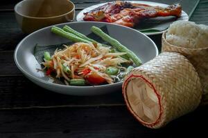 thaïlandais nourriture plat tous les deux dans Thaïlande et Asie, Papaye salade ou comme nous appel il somtum est complété avec grillé poulet et gluant riz avec Frais sautés. servi sur le noir en bois tableau. photo