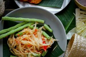 thaïlandais nourriture plat tous les deux dans Thaïlande et Asie Papaye salade ou comme nous appel il somtum est complété avec grillé poulet et gluant riz avec Frais sautés. servi sur le noir en bois tableau. photo