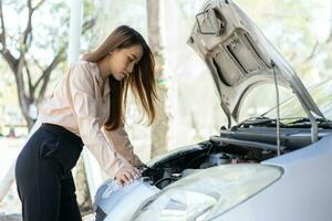 en colère asiatique femme en utilisant une téléphone intelligent vidéo conférence pour assistance après une voiture panne sur rue. concept de une véhicule moteur problème ou accident et urgence Aidez-moi de une professionnel mécanicien photo