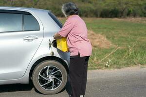 le voiture couru en dehors de gaz et bloqué à côté de le route dans banlieue et un personnes âgées asiatique femme utilisé une gallon de de rechange gaz à carburant le auto. une femme prépare une gallon de de rechange gaz à carburant avant en voyageant. photo