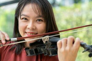 un attrayant femme apprentissage musicien pièces le violon à maison. compositeur création Chansons avec chaîne instruments. rêveur violoniste les doigts pressage cordes sur violon photo