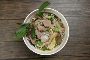 vietnamien poh du boeuf nouilles soupe bouillon avec du boeuf Balle pointe de poitrine tripes estomac les pièces été germer thaïlandais basilic citron vert dans bol sur en bois table photo