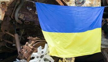 le nationale drapeau de Ukraine contre le Contexte de ruines et rouillé métal de détruit voitures. guerre dans Ukraine. une bleu jaune drapeau agitant dans le vent en dessous de le Soleil dans une bombardé ville. photo