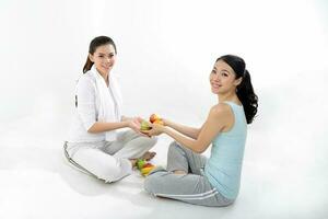 deux magnifique Jeune Sud est asiatique chinois en bonne santé faire des exercices exercice asseoir sur sol en portant des fruits vert Pomme Orange banane Regardez à caméra sur blanc Contexte photo