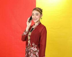 asiatique femme traditionnel bordeaux kebaya partager sur rouge Jaune papier Contexte parler utilisation téléphone téléphone intelligent photo