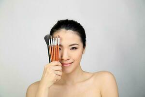 Jeune magnifique sud-est asiatique femme beauté mode maquillage lumière gris blanc Contexte en portant maquillage brosse plus de œil visage sourire photo