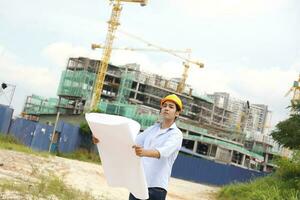 asiatique homme malais ouvrier ingénieur la gestion difficile chapeau sécurité casque à construction site en train de lire voyant plan plan photo