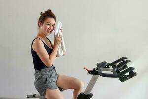 magnifique attrayant milieu âge sud-est asiatique femme exercice Stationnaire vélo cycle bicyclette dans une gymnase en bonne santé mode de vie Regardez vers l'avant transpiration serviette photo