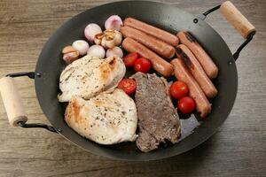 mélanger rencontrer la poêle poulet Sein du boeuf steak saucisse tomate oignon Ail pétrole frire gril sur métal friture la poêle deux bois manipuler sur rustique en bois Contexte photo