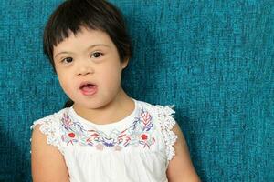 portrait de sud-est asiatique petit peu fille enfant séance sur bleu canapé Regardez content sourire pose. elle avoir vers le bas syndrome photo