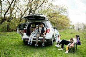 famille avec Trois des gamins contre voiture ouvert tronc sur pique-nique. photo