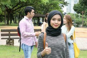 Jeune asiatique malais chinois homme femme Extérieur parc marcher supporter étude parler discuter point portable fichier livre sac à dos femelle Regardez vers l'avant les pouces en haut photo