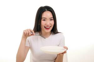 magnifique Jeune Sud est asiatique femme faire semblant agissant posant en portant vide fourchette cuillère blanc assiette dans main manger goût Regardez voir blanc Contexte sourire content photo