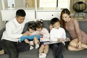 Parents enfant famille père mère fille fils asseoir sur canapé en train de lire l'écriture étude enseignement photo