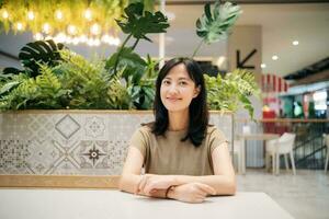 souriant magnifique asiatique femme séance dans cafétéria à achats centre commercial. photo