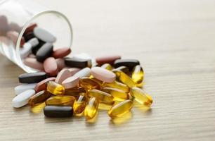 Capsules d'huile de poisson et suppléments de multivitamines hors du petit verre sur la table en bois avec copie espace photo