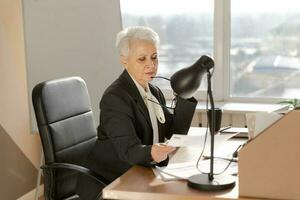 sur de soi élégant européen milieu vieilli Sénior femme en train de lire financier rapport Documentation statistiques. élégant plus âgée mature Années 60 gris aux cheveux Dame femme d'affaires dans bureau. patron chef professeur. photo