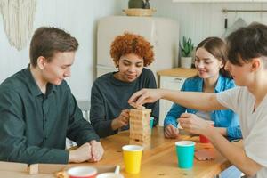 Accueil faire la fête. copains dépenses temps ensemble en jouant dans planche Jeu crash en bois la tour à maison. content diverse groupe ayant amusement ensemble intérieur. mixte course Jeune copains meilleur copains profiter fin de semaine. photo