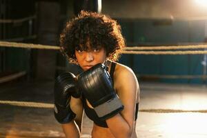 tollé indépendant fille pouvoir. en colère africain américain femme combattant avec boxe gants à la recherche sérieux agressif permanent sur boxe anneau. fort puissant combattant fille formation coups de poing. photo