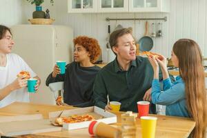 Accueil fête copains dépenses temps ensemble ayant amusement en riant communicant à maison. content diverse groupe en mangeant Pizza en buvant Bière ou limonade. mixte course Jeune copains meilleur copains profiter fin de semaine. photo