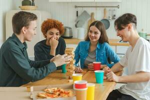 Accueil faire la fête. copains dépenses temps ensemble en jouant dans planche Jeu crash en bois la tour à maison. content diverse groupe ayant amusement ensemble intérieur. mixte course Jeune copains meilleur copains profiter fin de semaine. photo