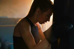 femmes soi la défense fille pouvoir. fort femme combattant repos après bats toi formation sur boxe anneau. fort fille fatigué après perforation boxe sac. formation journée dans salle de sport. force en forme corps faire des exercices entraînement. photo