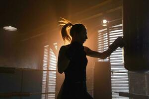 femmes soi la défense fille pouvoir. fort femme combattant formation poinçons sur boxe anneau. en bonne santé fort fille perforation boxe sac. formation journée dans boxe salle de sport. force en forme corps faire des exercices entraînement. photo