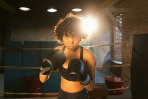 tollé indépendant fille pouvoir. en colère africain américain femme combattant avec boxe gants à la recherche sérieux agressif permanent sur boxe anneau. fort puissant combattant fille formation coups de poing. photo